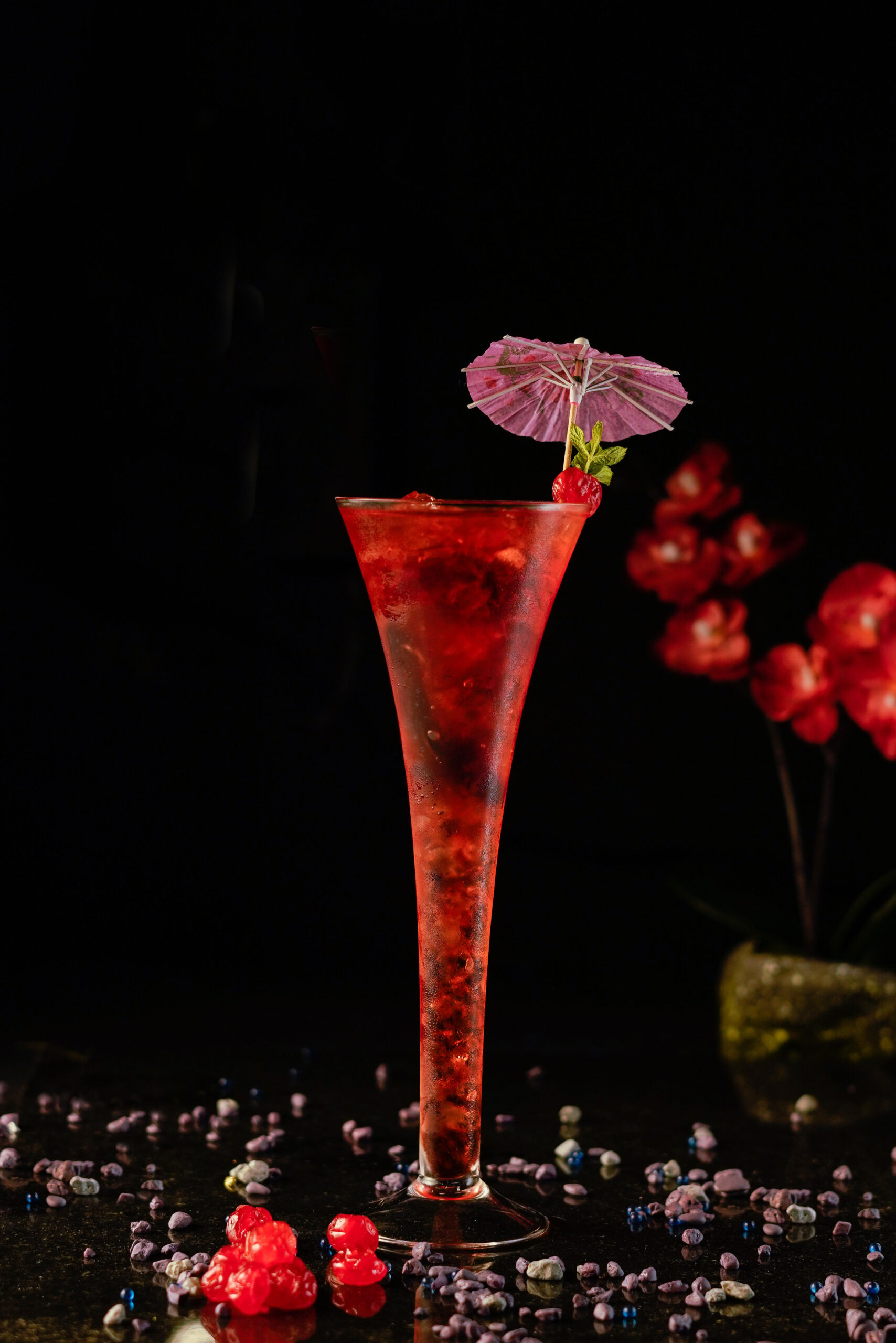 Red cocktail inside a long trumpet champagne glass garnished with an umbrella cocktail pick