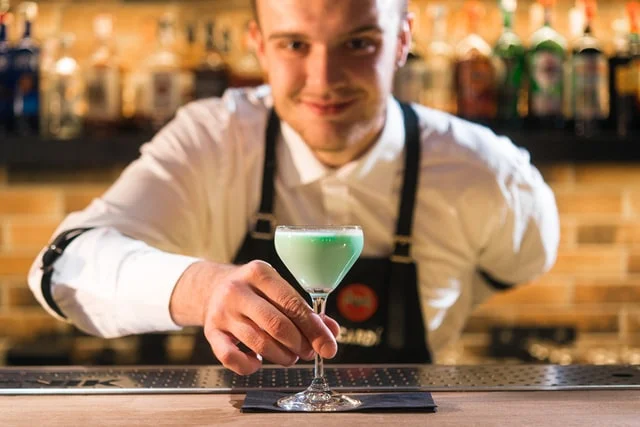 Bartender holding a coupe glass containing a green cocktail