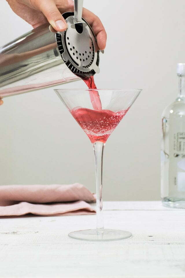 Red cocktail being strained into a martini cocktail glass