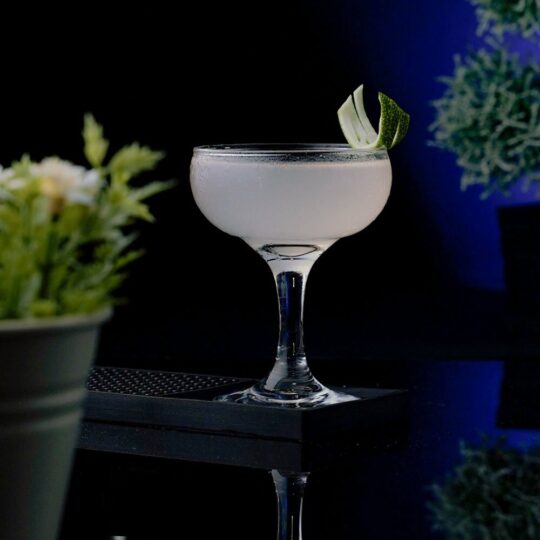 White Cocktail in a Coupe Glass garnished with a Lemon Peel