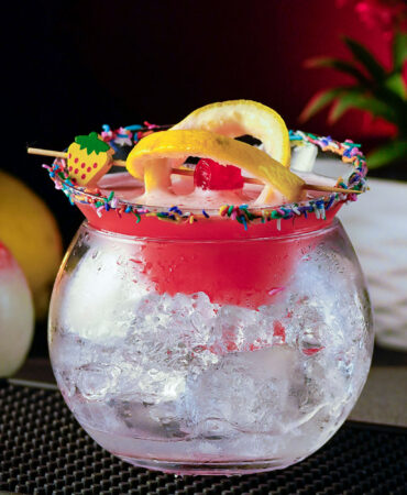 Pink cocktail inside a two parts glass garnished with lemon wheels on a cocktail pick