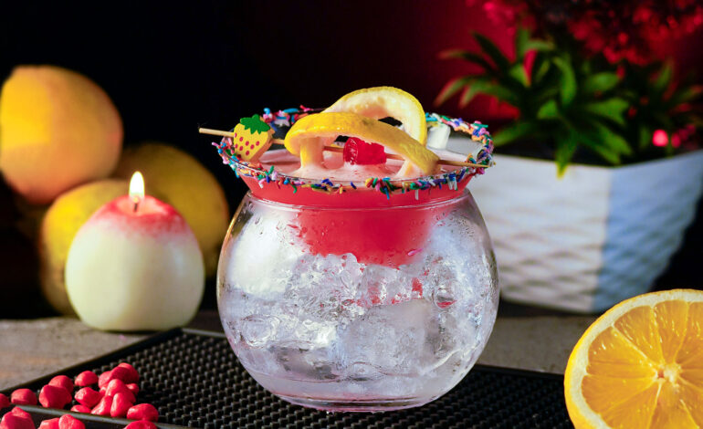 Pink cocktail inside a two parts glass garnished with lemon wheels on a cocktail pick