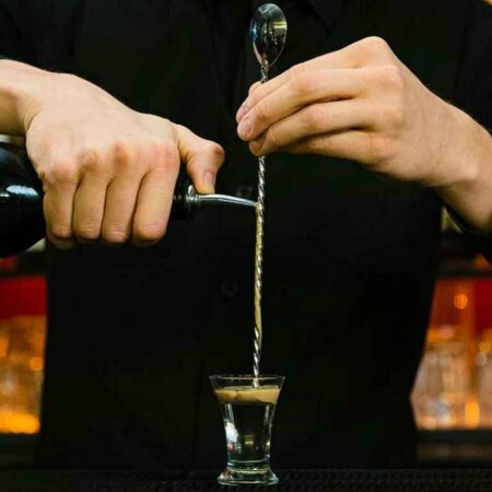 Bartender layering a shot glass by pouring onto the disk tail spoon