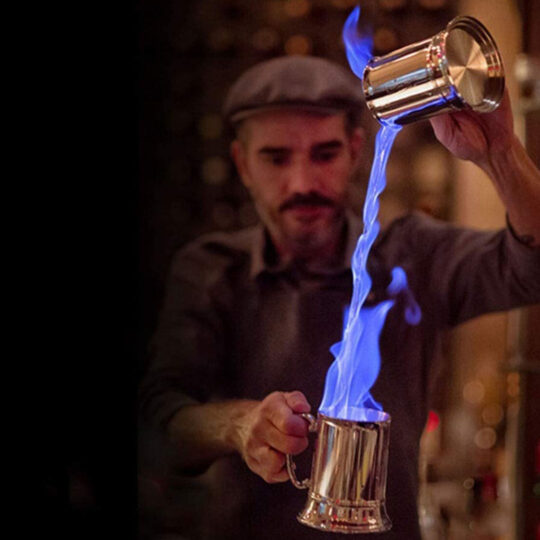 Bartender Pouring a beverage that is set on flame with two The Double Trouble Mugs