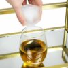 Hand placing a square ice cube into a whisky glass
