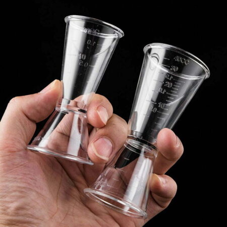 Hand holding two lucent cocktail jiggers for bartending