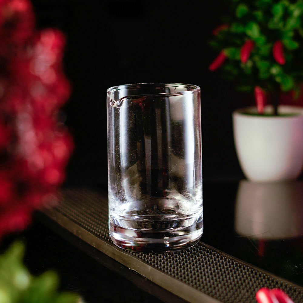 Clear Sky Mixing Glass Laying on the long rectangular rubber bar mat around a dark and red background