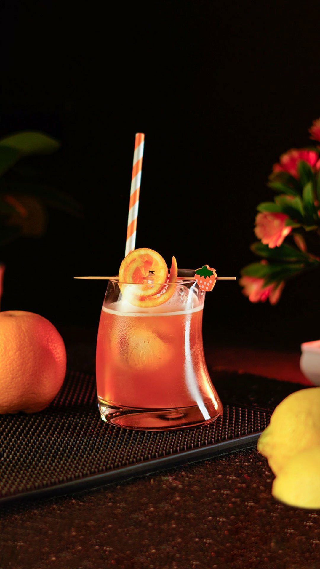 Orange cocktail inside a hunched short glass garnished with an orange peel on a cocktail pick