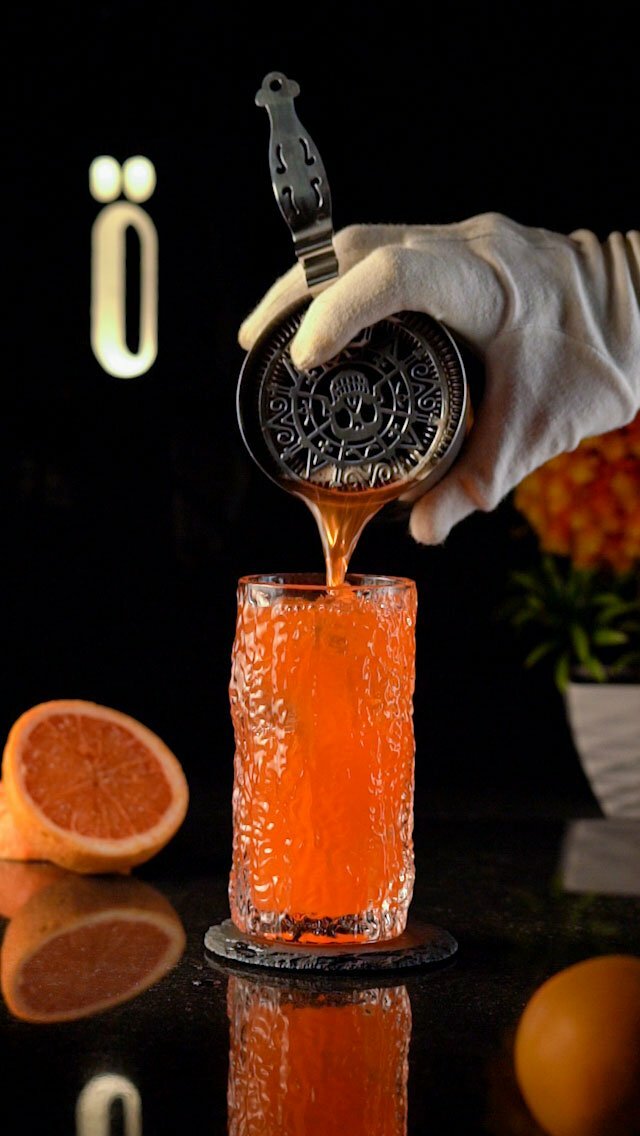 Orange cocktail being poured into a carved highball glass with a texture