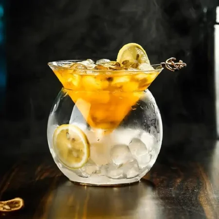 Elegant Holy Cone glass with amber cocktail, ice, garnished with lemon on dark backdrop.