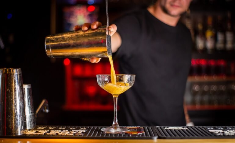 Bartender straining a cocktail into a coupe glass using a shaker and strainer