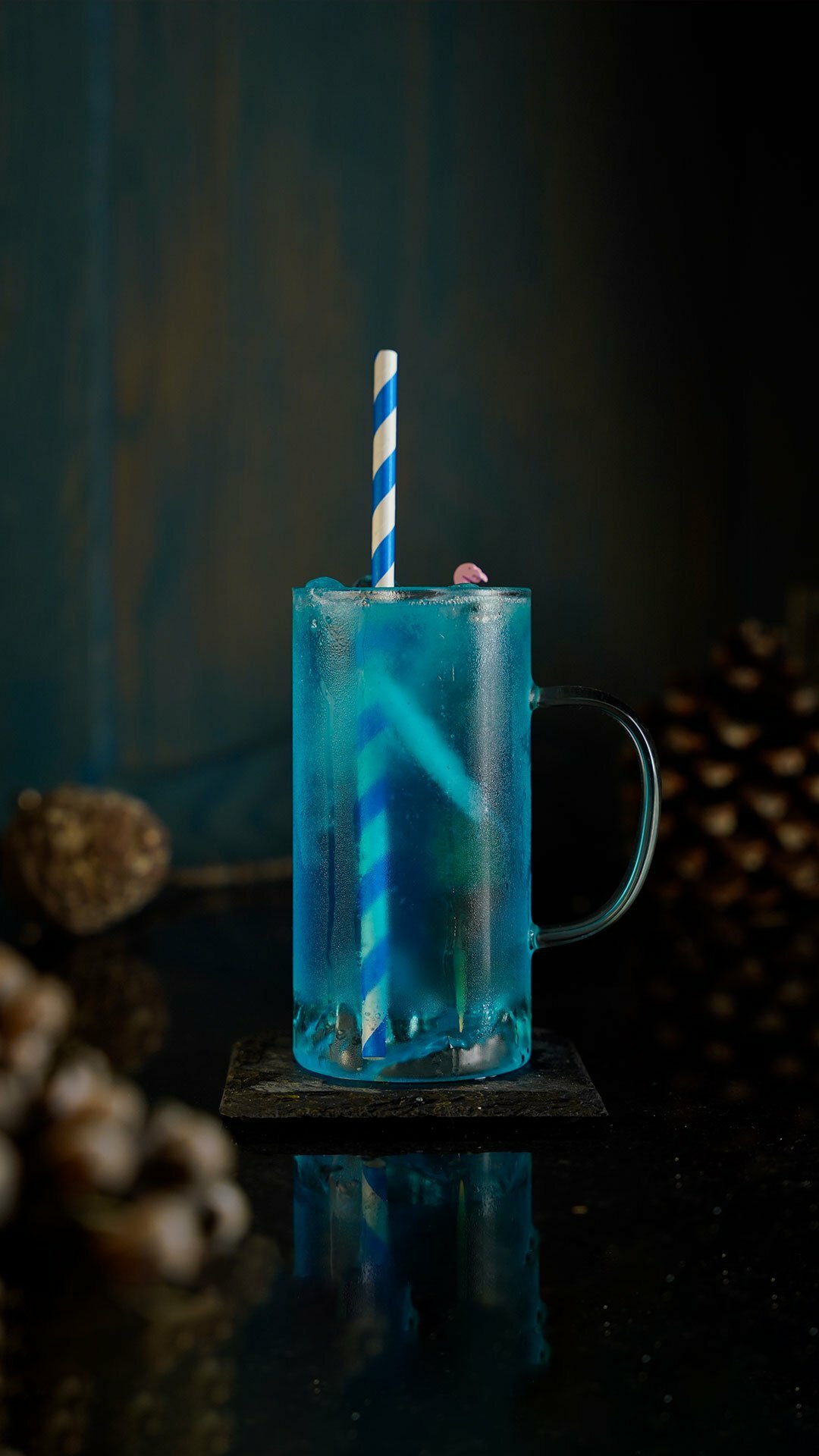 Blue cocktail inside a collins glass with a blue straw inside it