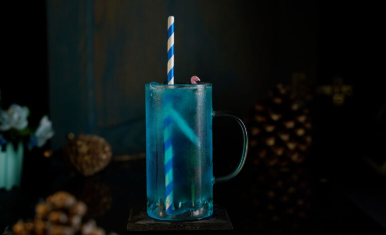 Blue cocktail inside a collins glass with a blue straw inside it