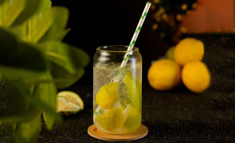 Cocktail with lemon slices filled inside a glass can with lemons and leaves around the background