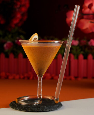 Orange Cocktail named French Martini inside an exquisite glass with a built in straw around a red background