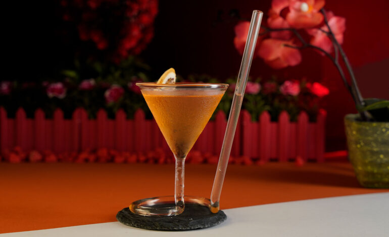 Orange Cocktail named French Martini inside an exquisite glass with a built in straw around a red background