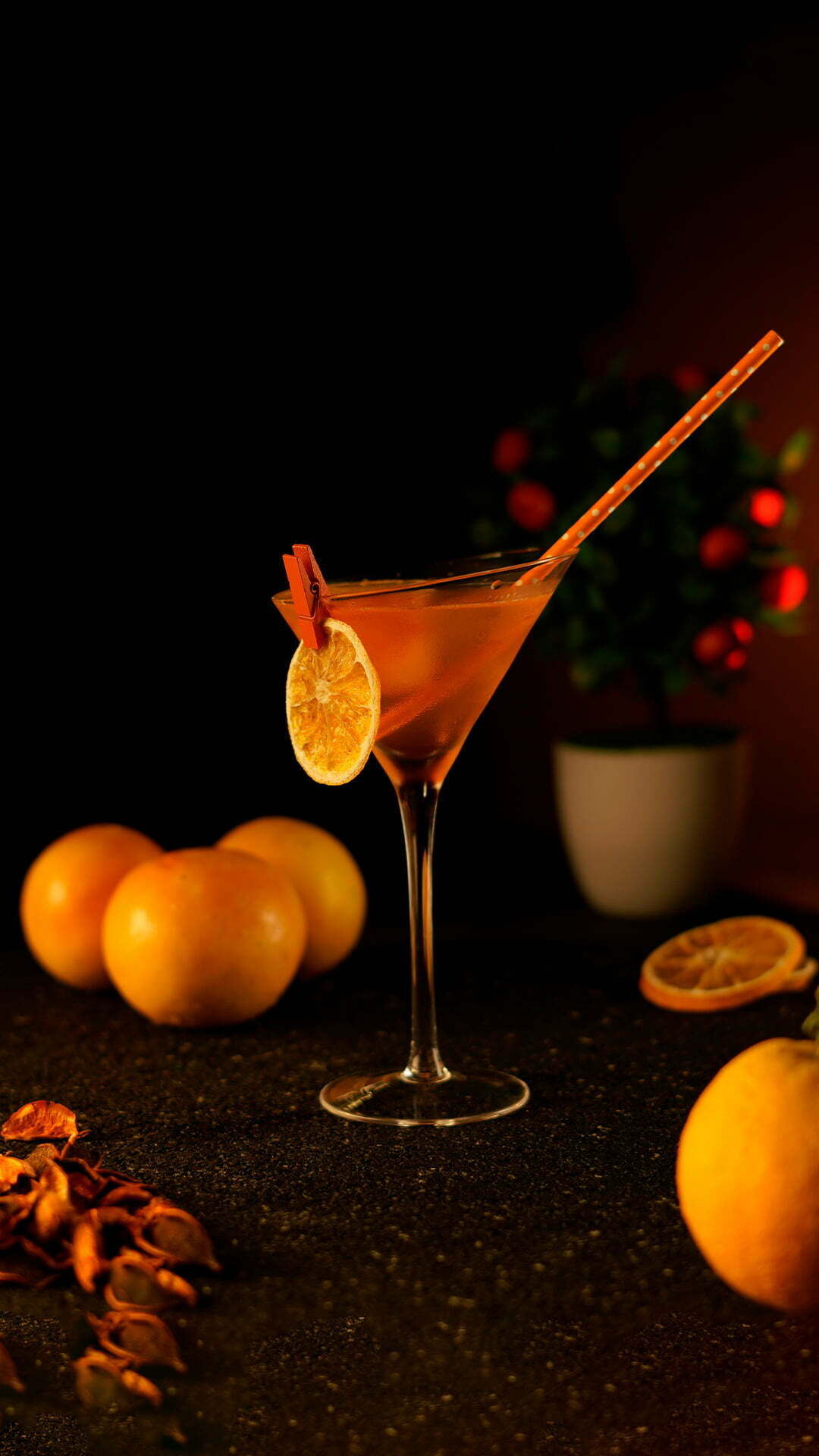 Orange cocktail in a martini glass placed in a dark background next to oranges