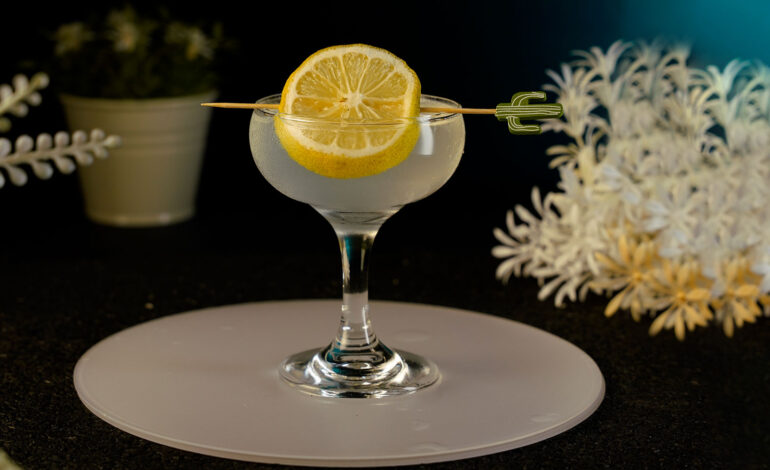 Gin cocktail served in a small coupe glass garnished with a lemon wheel on a cocktail pick