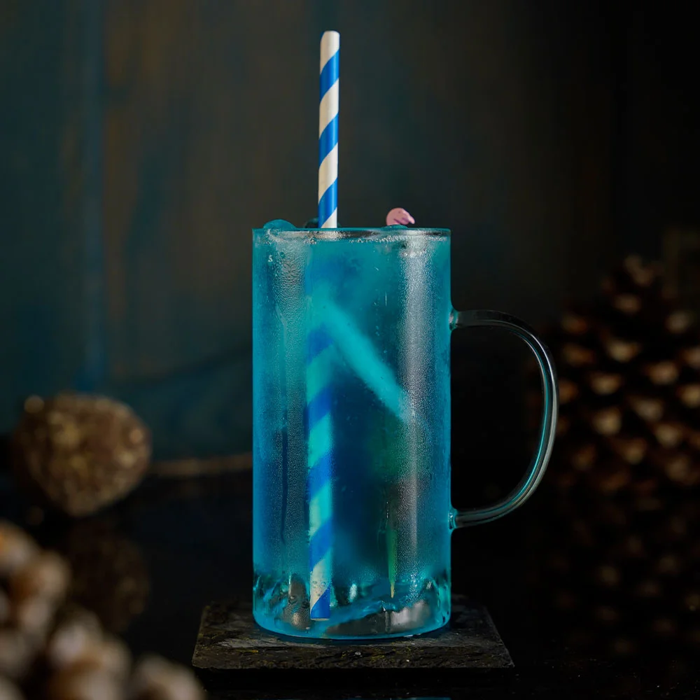 Collins Glass with a Handle that has a beautiful mountain design on it's bottom filled with a blue bright cocktail