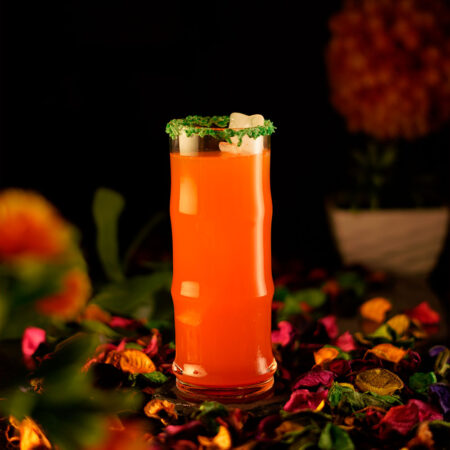 Collins glass filled with orange cocktail around a colorful background