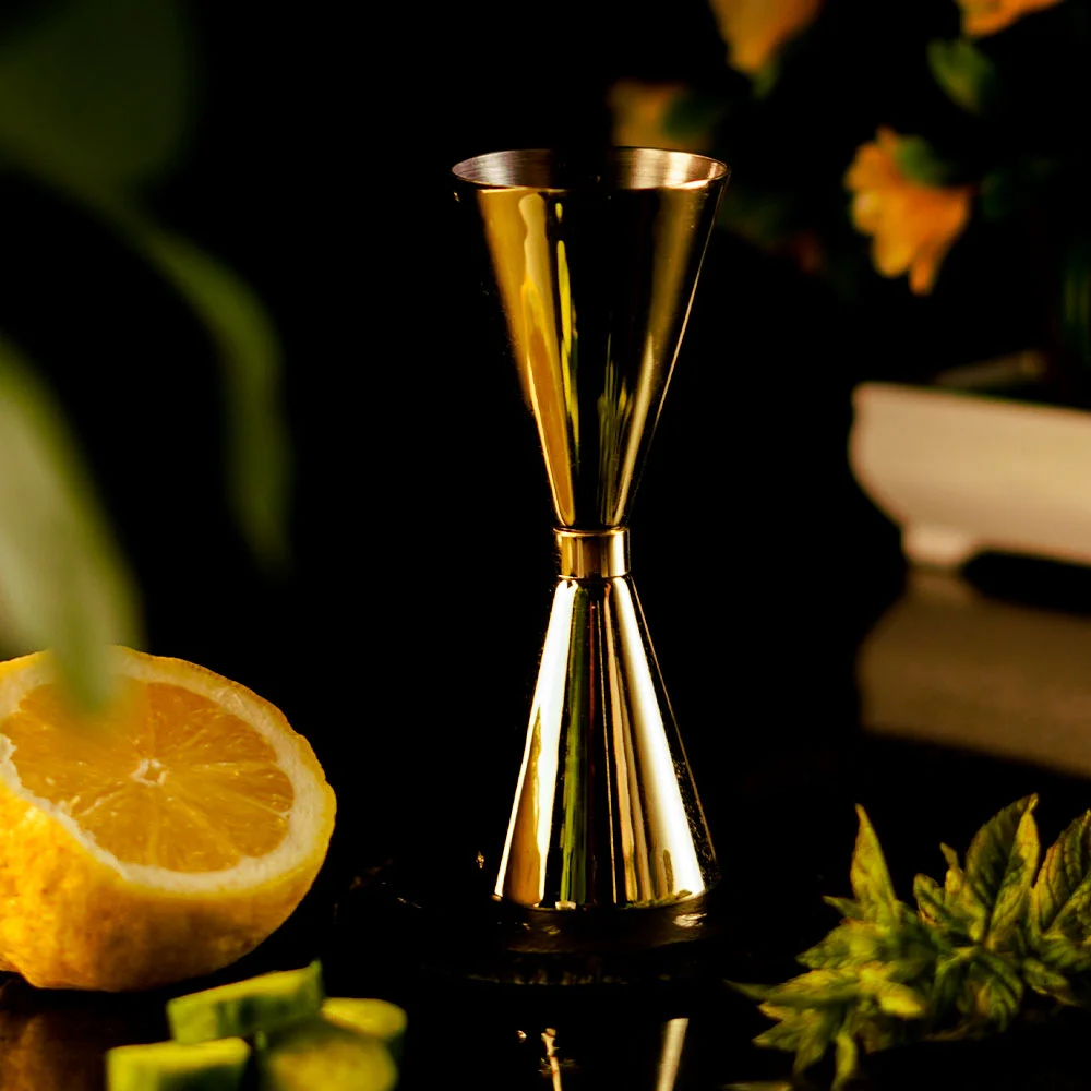 Gold Japanese Bartending Jigger around a dark background with mint next to it