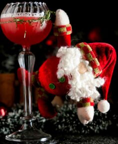 Red Cocktail inside a Goblet cocktail glass with a Santa Clause hanging on it