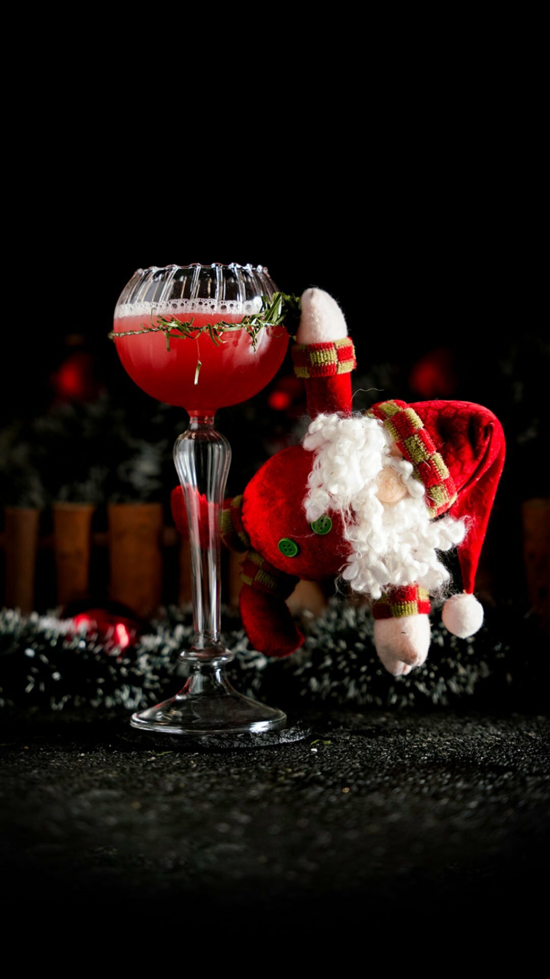 Red Cocktail inside a Goblet cocktail glass with a Santa Clause hanging on it