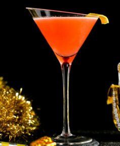 Orange Cocktail inside a Tilted Martini Glass around celebration gold props