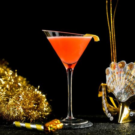 Orange Cocktail inside a Tilted Martini Glass around celebration gold props