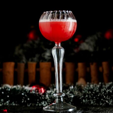 Red Cocktail inside a Goblet cocktail glass around a Christmas Background