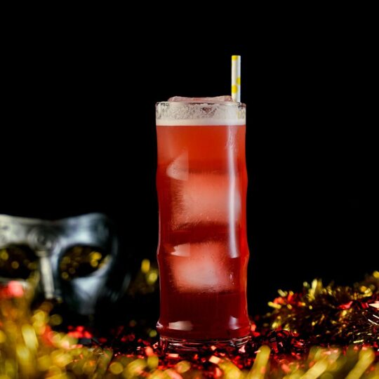 Red Cocktail inside a Collins glass around New Year's Eve celebration Background