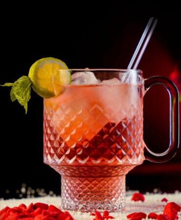 Red Refreshing Cocktail inside a Large Carved Beaker Mug garnished with a Lemon Wheel and a Mint Sprig