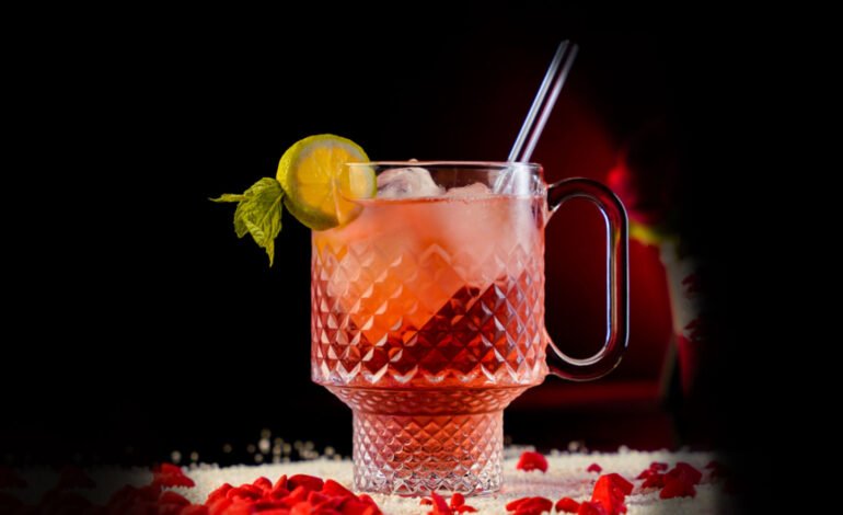 Red Refreshing Cocktail inside a Large Carved Beaker Mug garnished with a Lemon Wheel and a Mint Sprig