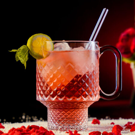 Red Refreshing Cocktail inside a Large Carved Beaker Mug garnished with a Lemon Wheel and a Mint Sprig