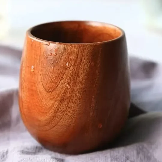 A handcrafted wooden cup from The Artisan Sip, placed on a striped cloth with visible wood grain and small droplets of liquid on the side, indicating condensation from a cold beverage.