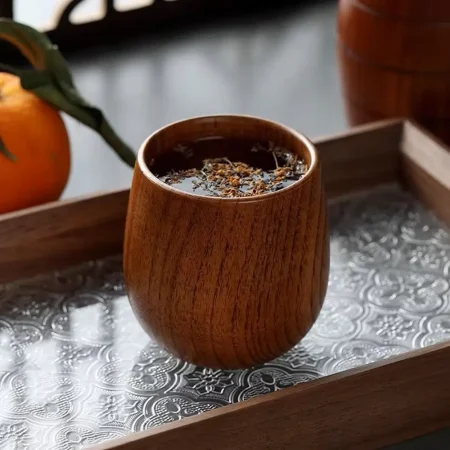 A handcrafted wooden tumbler from The Artisan Sip, filled with a beverage and resting on an ornate metallic tray, showcasing the rich, natural wood grain and artisanal quality.