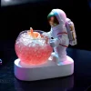 Rounded 250 ml capacity glass with playful astronaut design hugging the side, filled with pink beverage on illuminated base