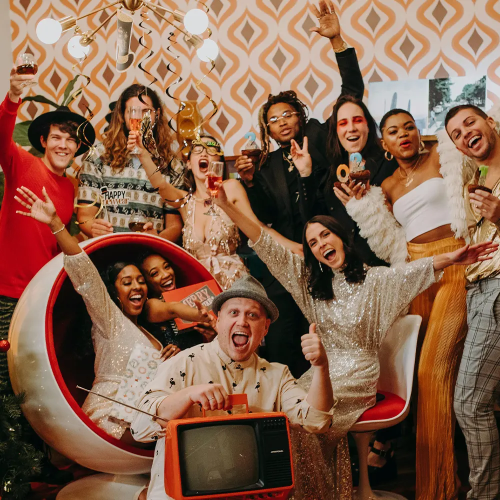 A group of individuals enjoying a festive celebration with decorative lights and a vintage television set, highlighting the versatility and fun of premium drinkware for any event.