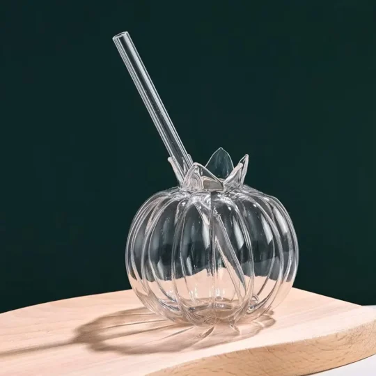 Hand-blown Pumpkin Twist Glass made from heat-resistant borosilicate, featuring a pumpkin design with ribbed sections and a leaf-like detail on top, placed on a wooden surface against a dark green background.