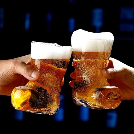 Two hands clinking cowboy boot-shaped beer glasses filled with amber beer and frothy white head, set against a dark background with blue digital patterns.