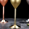 Close-up view of the stems of two stainless steel champagne glasses, one with a gold finish and the other with a copper finish, showing condensation droplets.