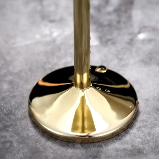 Close-up view of the stem of a gold-finished stainless steel champagne glass, showing condensation droplets and a reflective surface.