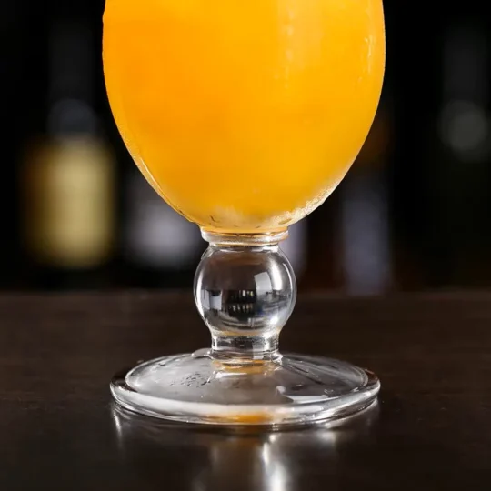 Close-up of the stem and base of a 420 ml Tempest Twist Glass with an orange beverage, highlighting its elegant design.