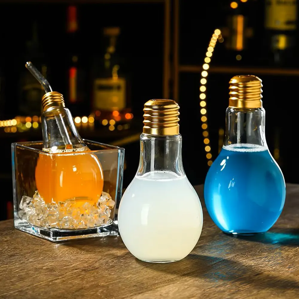 Three light bulb-shaped beverage containers filled with orange, milky white, and blue liquids, set on a bar with blurred lights and bottles in the background.