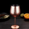 Close-up of a copper metallic wine glass with a smooth finish, filled with ice and garnished with mint leaves and a cherry, set against a dark background.