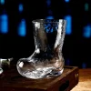 Clear cowboy boot-shaped glass placed on a wooden surface with a dark background and blurred blue lights, highlighting its unique design