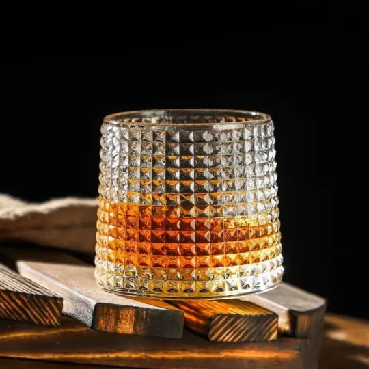 Dimpled whisky glass from the Sip & Swirl Collection, featuring unique dimple-like indentations and a rotating base, filled with amber whisky.