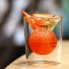 A Dual Illusion Tumbler with a clear outer square silhouette and a textured orange sphere in the center, garnished with citrus slices and a green herb, perfect for cocktails.