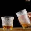 Two frosted silhouette glasses with a unique textured finish, one half-filled with amber liquid, held against a dark background.