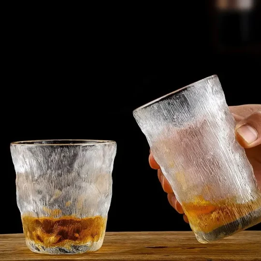 Two frosted silhouette glasses with a unique textured finish, one half-filled with amber liquid, held against a dark background.